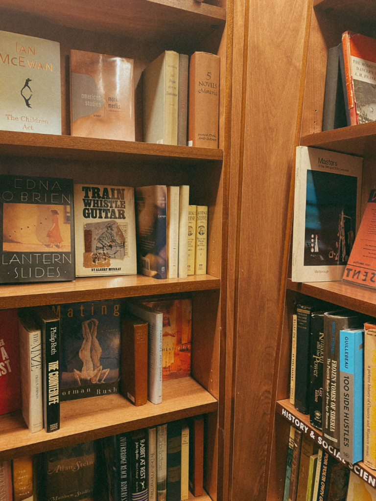 A wooden bookshelf lined with books including Edna O'Brien's Lantern Sands at McNally Jackson Books in South Street Seaport, New York City.