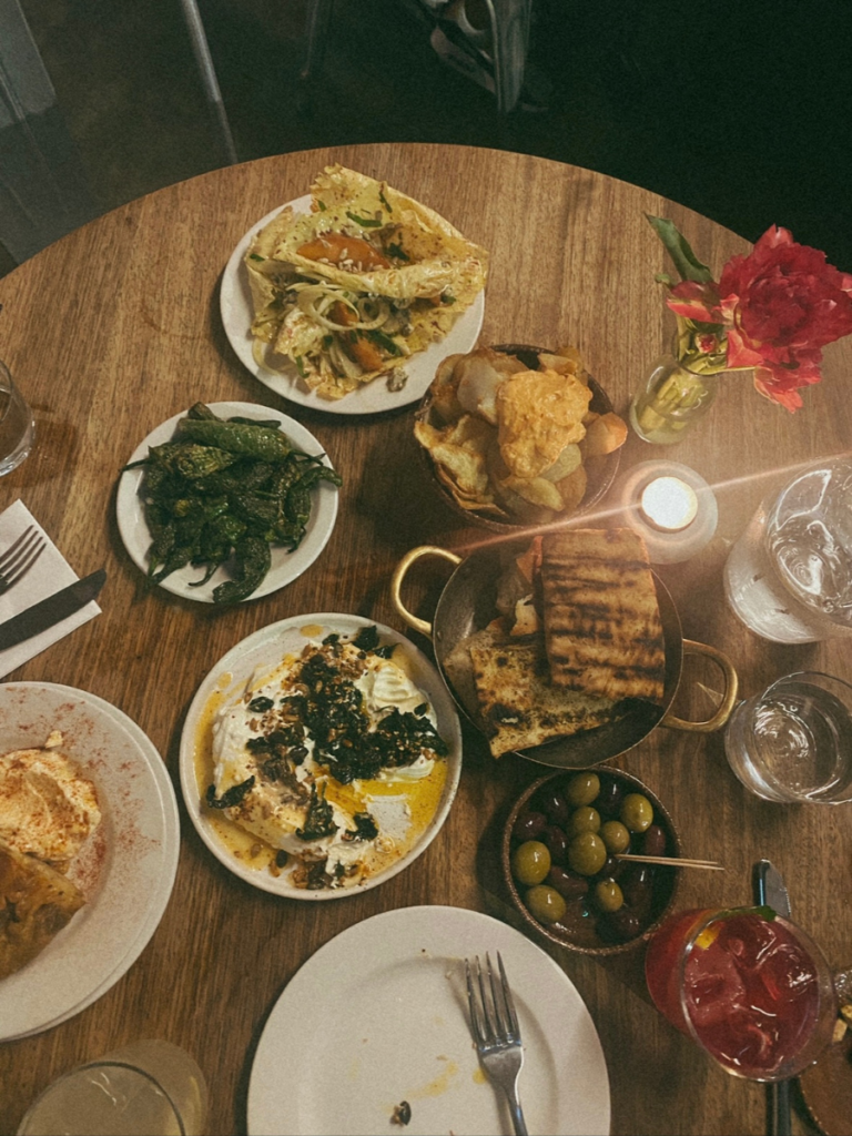 A shared plates dinner around a wooden table with friends, with padron peppers, flatbread and olives and pink drinks at Morito Hackney Road, London