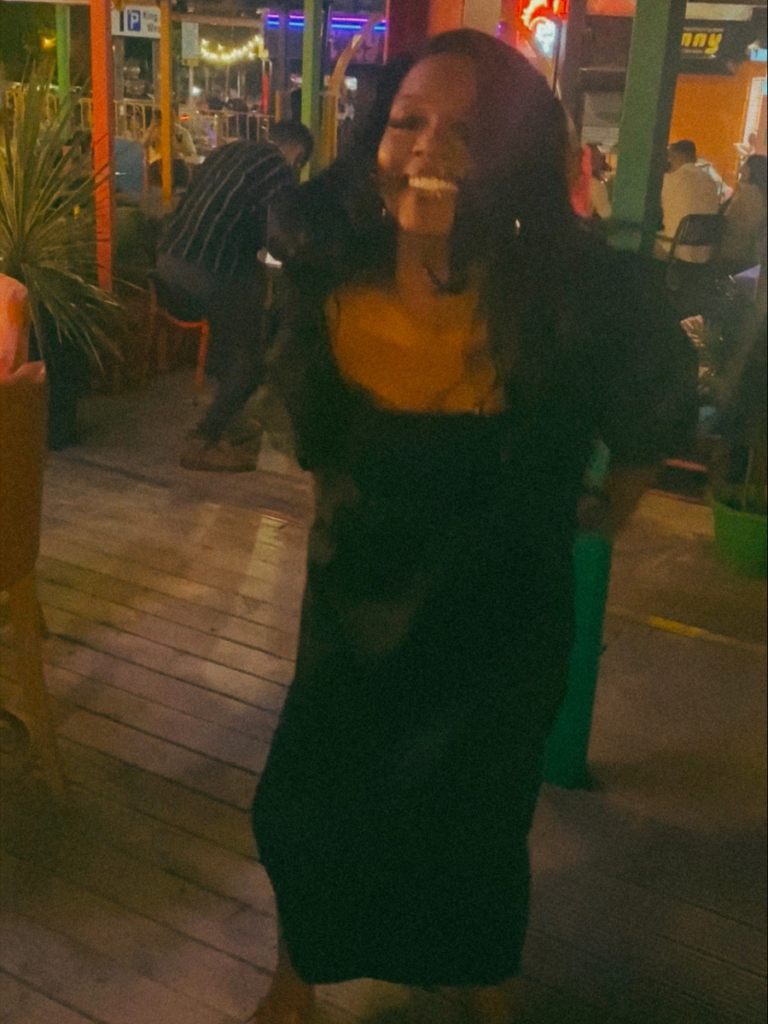 A black woman dancing by herself in a black dress. 
