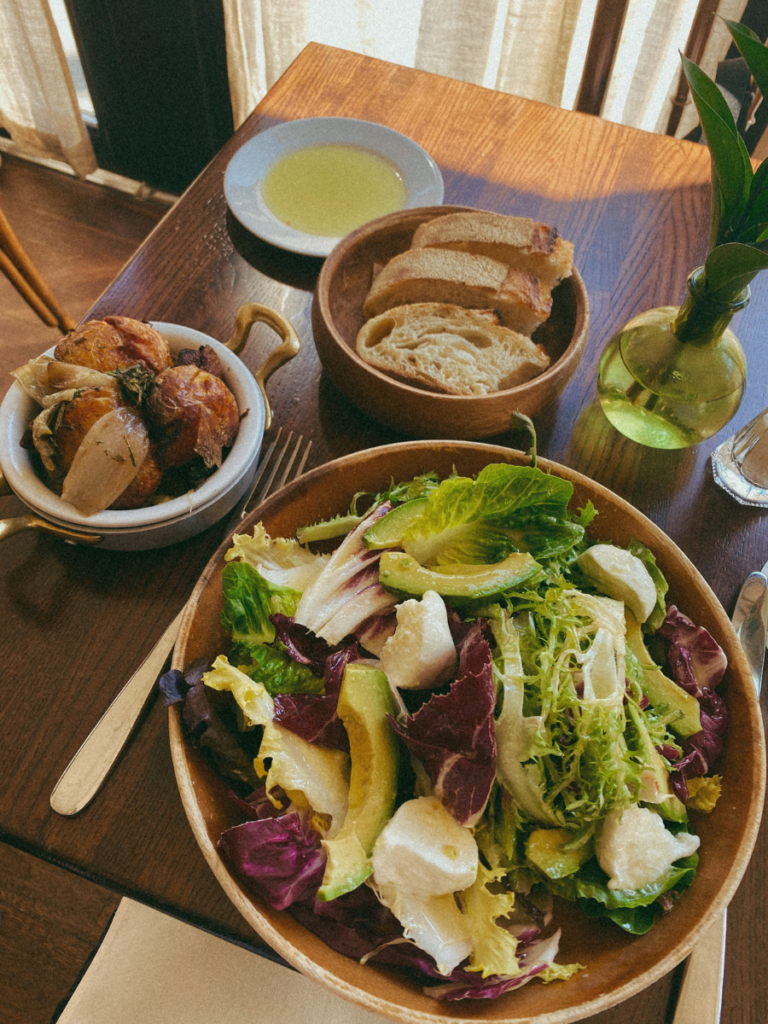 A huge salad with avocado and mozzarella, roast potatoes and fresh bread with olive oil at a wooden table at the restaurant Felice in New York City.